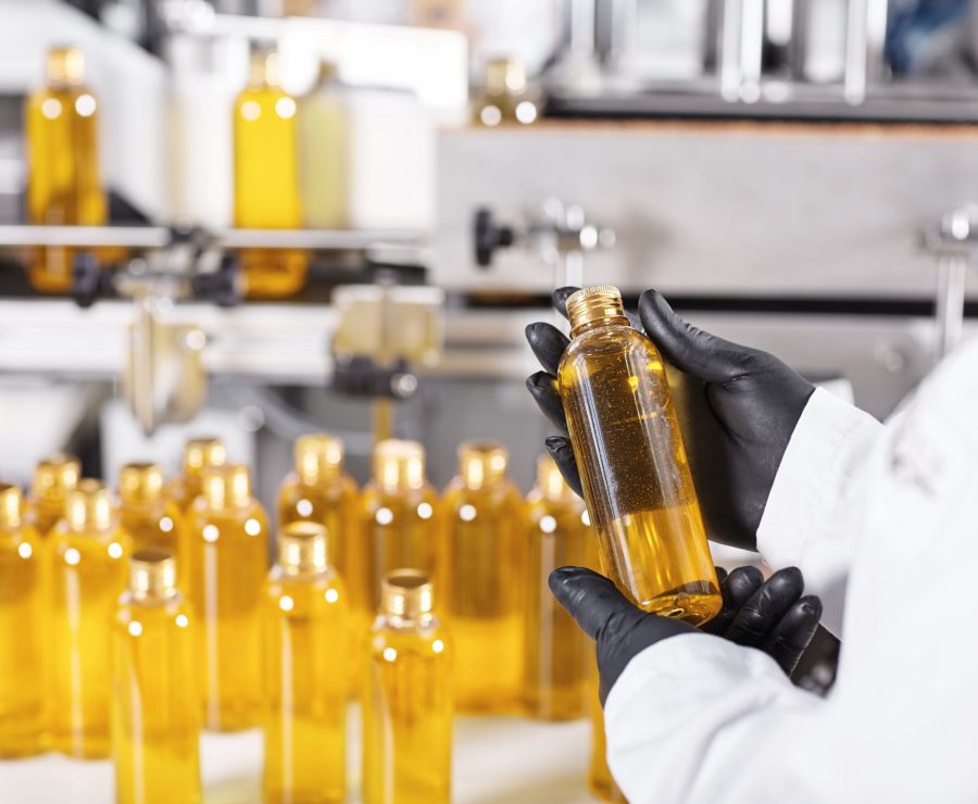 Medical production, pharmacy and healthcare industry. Employee wearing protective clothes holding bottle with golden substance in his hands, conducting quality control of end product at factory